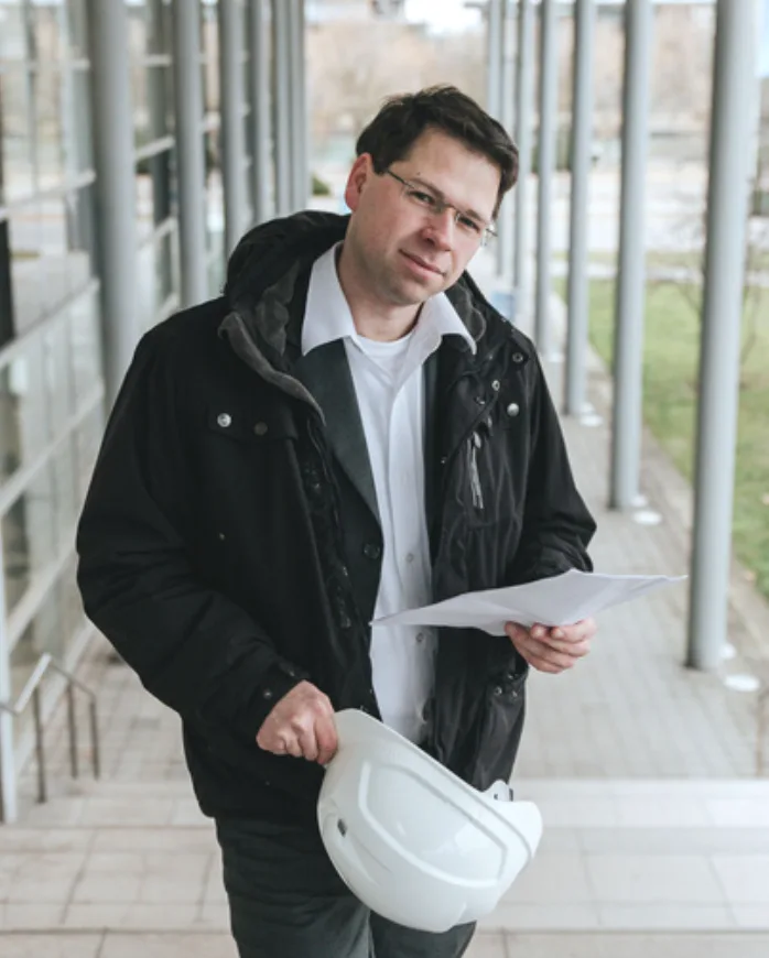 Portrait eines Unternehmers mit Schutzhelm und Unterlagen vor einem Bürogebäude
